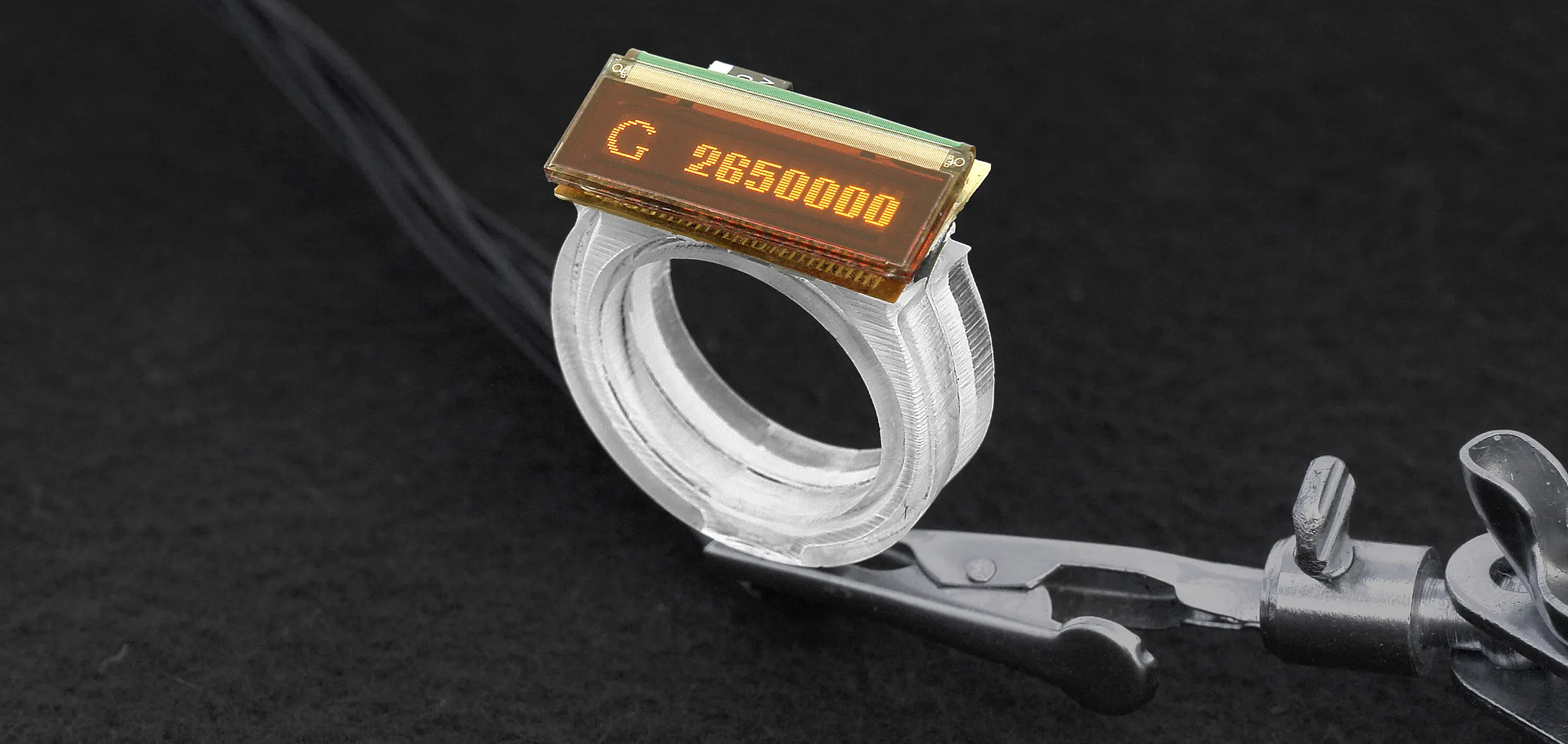 A glass ring with a small orange LED screen. The screen displays G2650000.