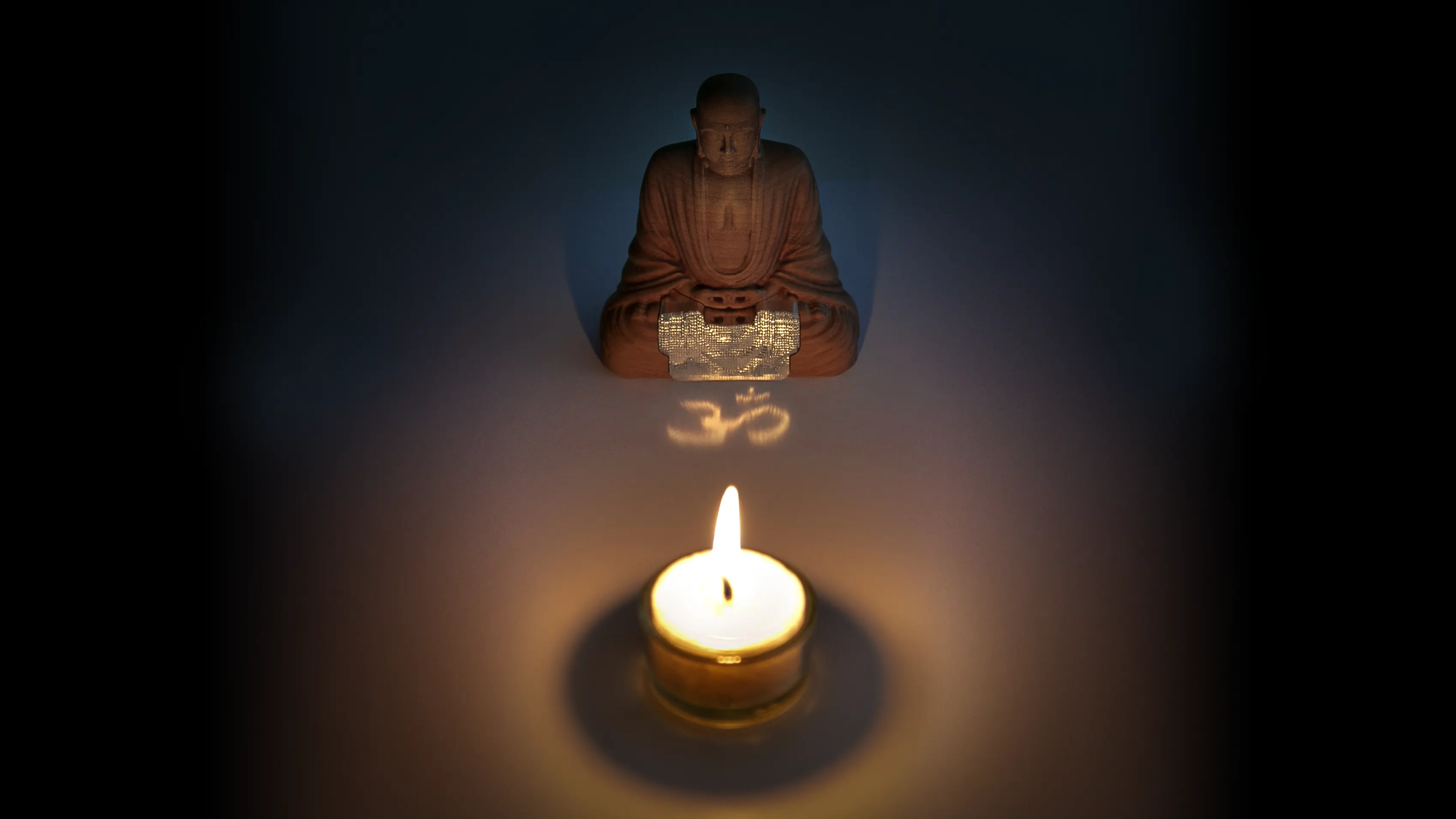A Buddha figure sits in front of a candle and the light the is reflected from it draws the Ohm Symbol to the table surface.