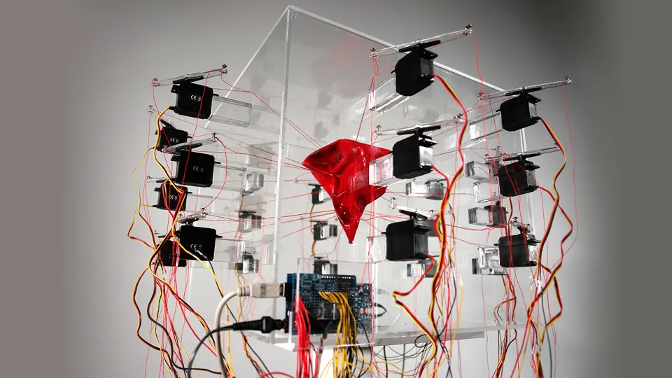 A glass cube with a red latex object inside and a lot of motors and cables