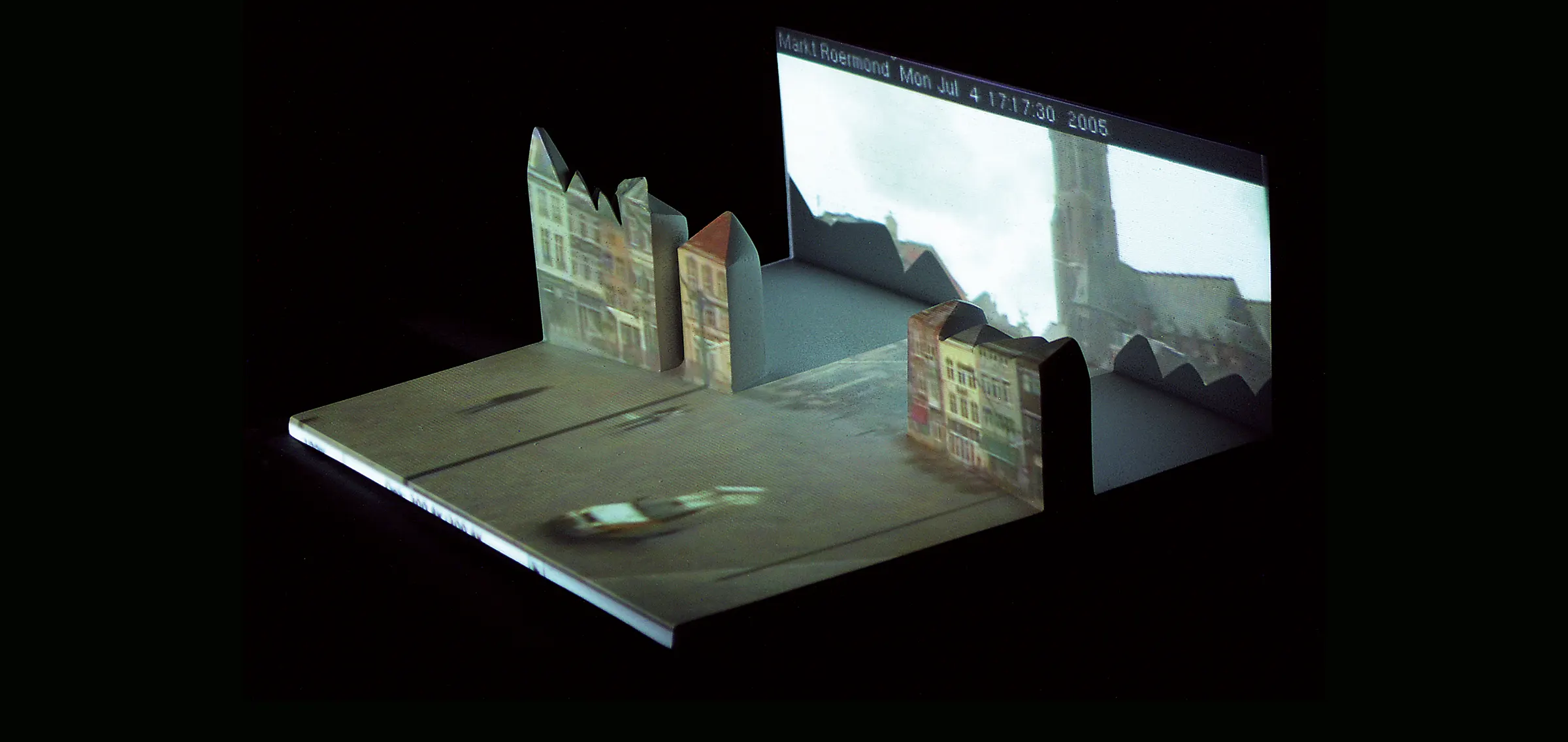 A few folded-paper like white concrete sculptur with projected images of facades on it. 